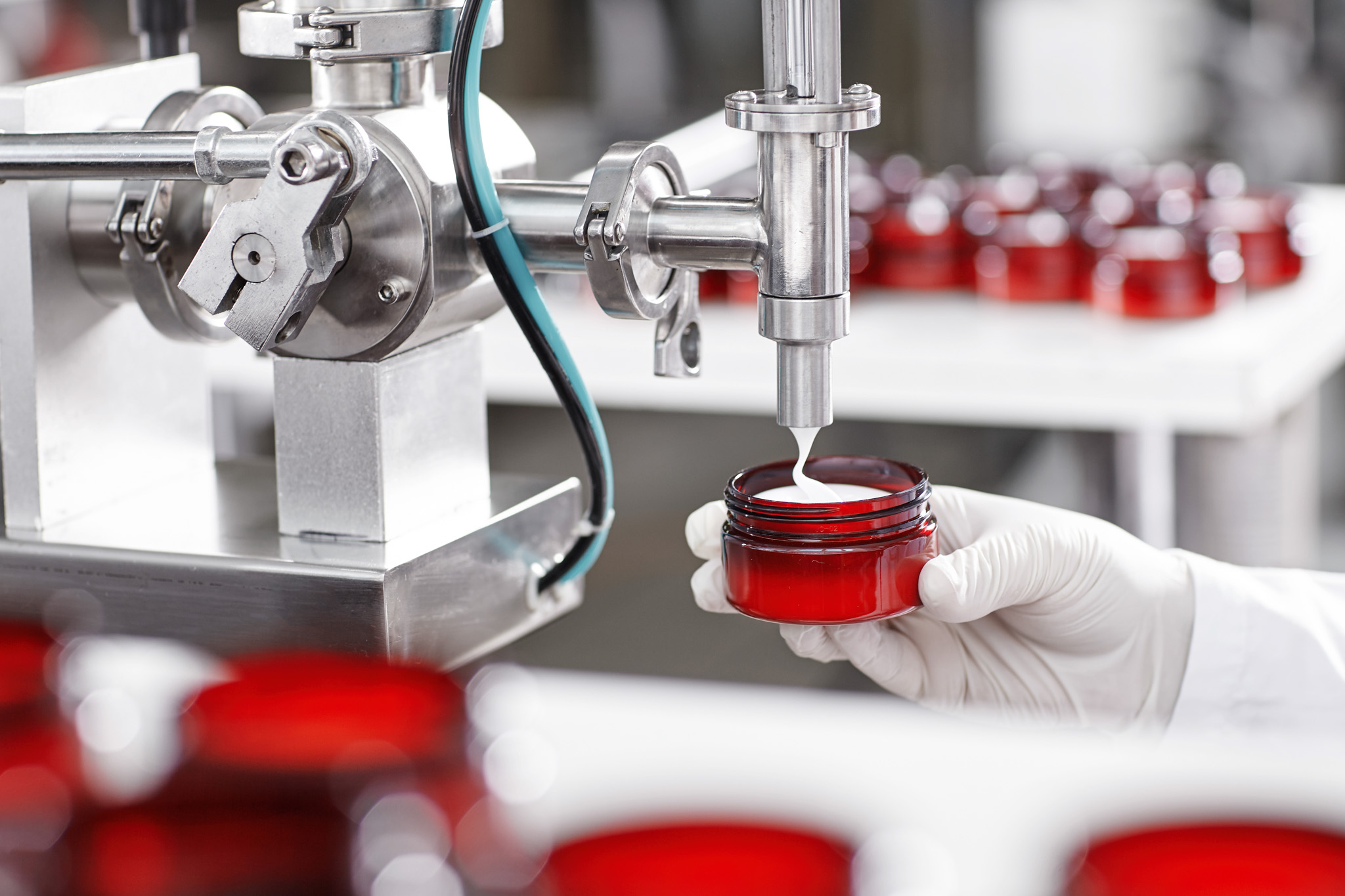 Production and packaging of cosmetics products. Cropped shot of factory worker in gloves and gown holding plastic jar, filling it with white face or body cream